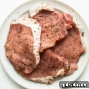 Pork chops on a plate, seasoned and ready for tenderizing and stuffing.