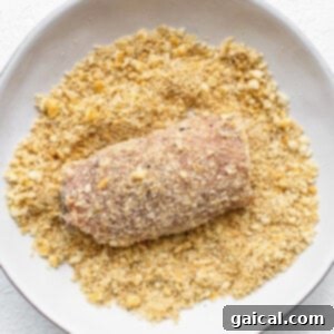 Dredging a stuffed pork chop in a bowl of seasoned Ritz cracker crumbs for a crispy coating.