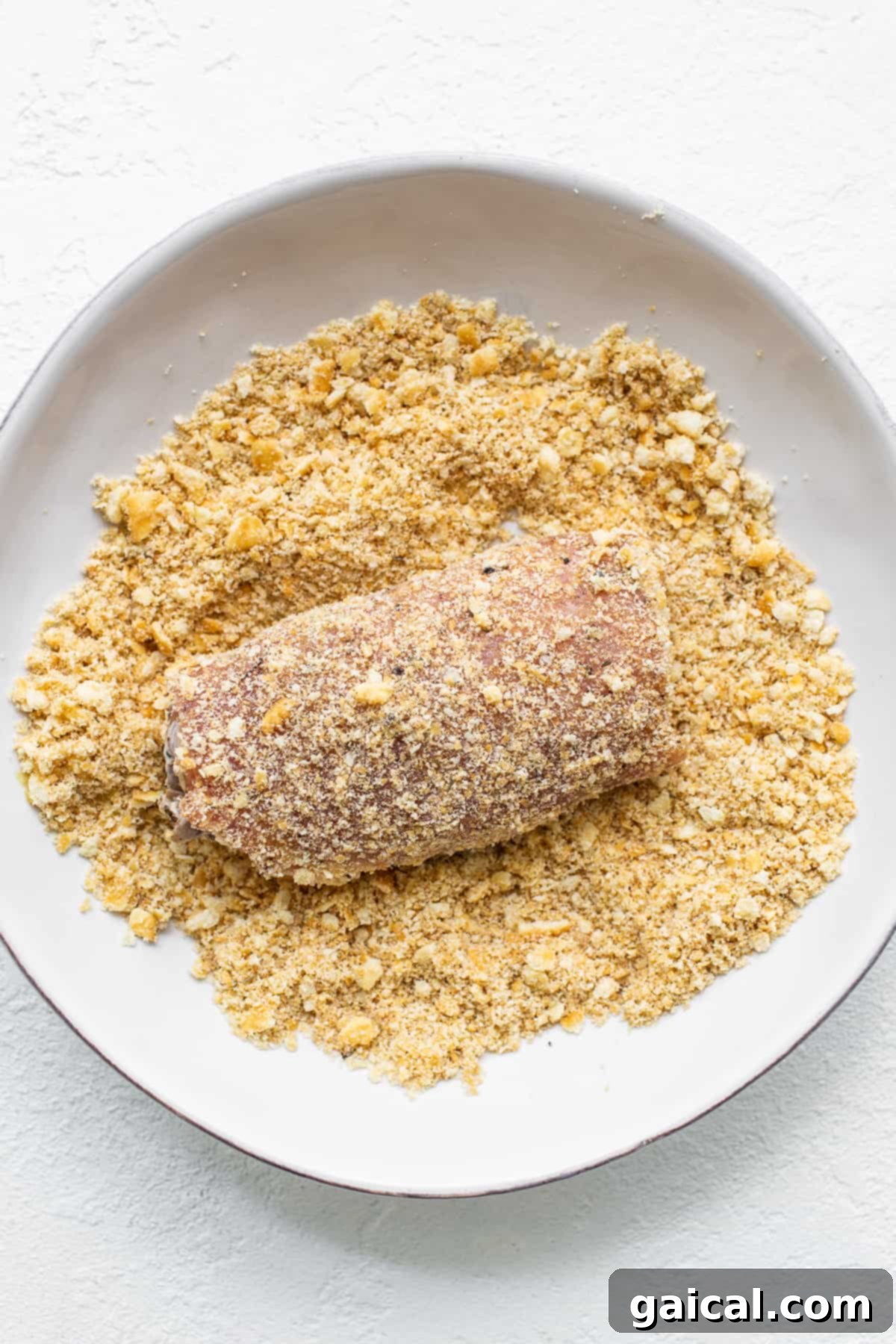 Achieving Perfect Crispy Coating on Stuffed Pork Chops Hand carefully dredging a stuffed pork chop in a bowl of Ritz cracker crumbs.