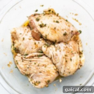 Chicken thighs marinating in a bowl with herbs and spices.