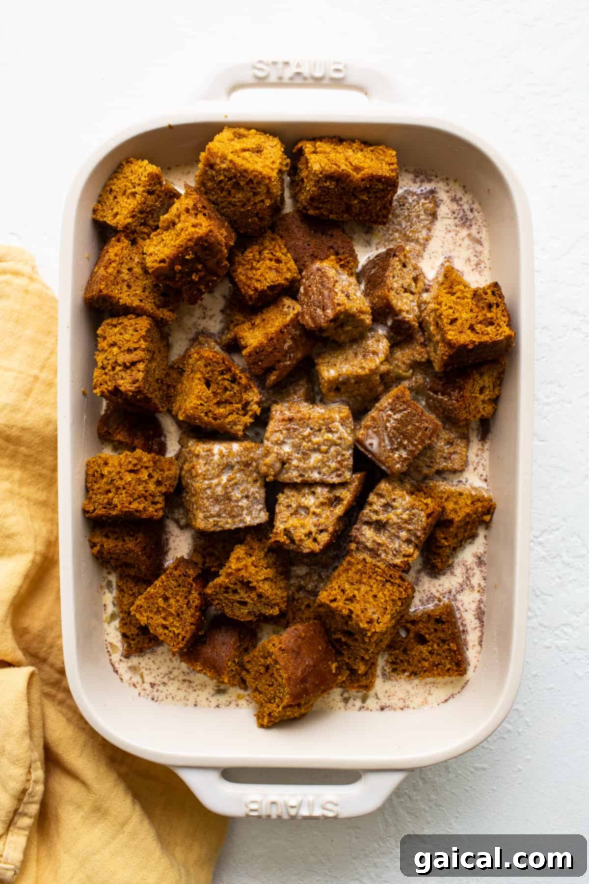 Pumpkin Bread Soaking in Custard Pumpkin bread pudding cubes thoroughly soaking in rich egg custard mixture in a clear glass bowl, ensuring maximum flavor absorption.