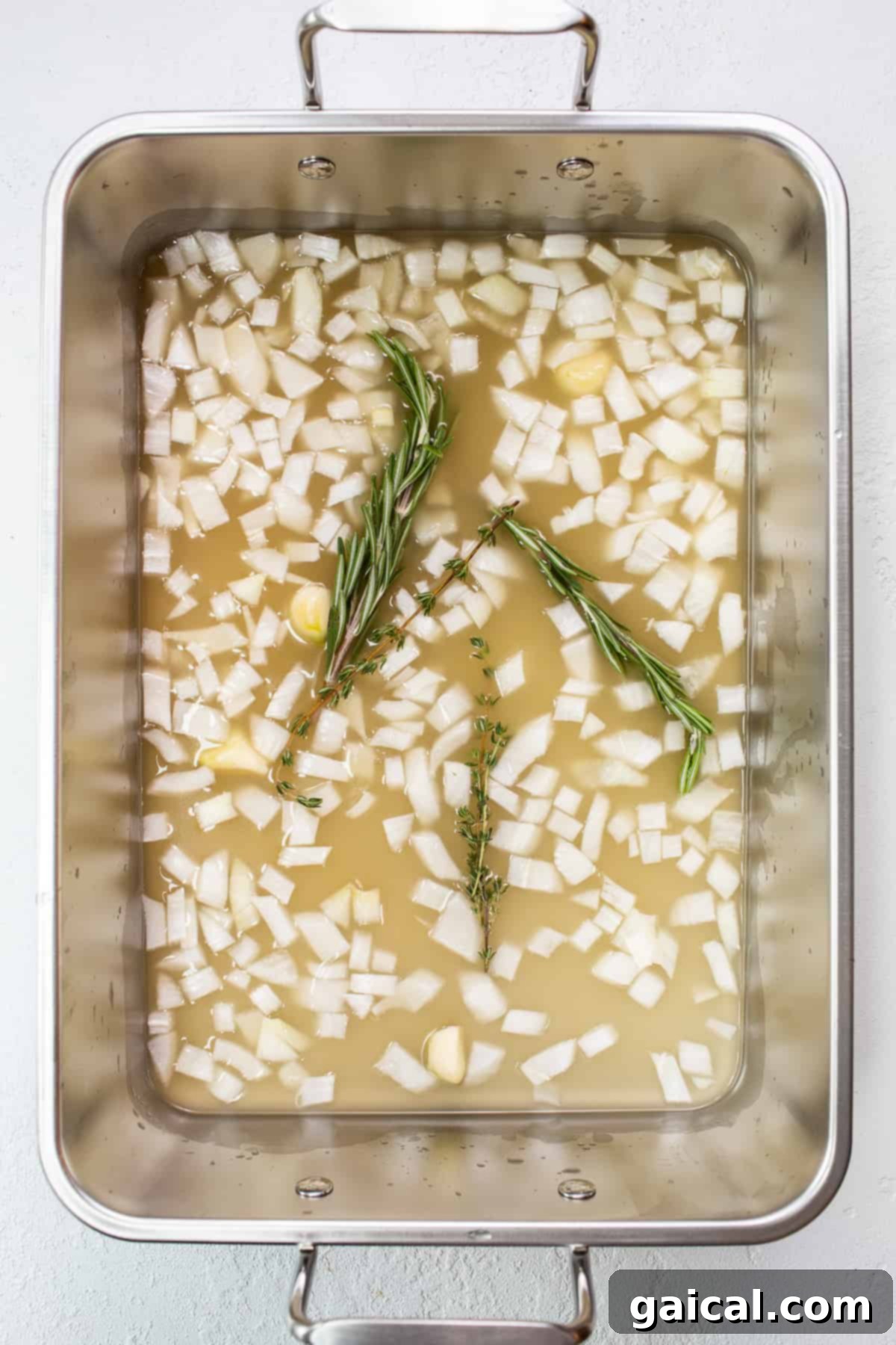 The Ultimate Thanksgiving Turkey Guide 6 A close-up of a rich, golden basting liquid simmering in the bottom of a roasting pan, infused with herbs, onions, and garlic.