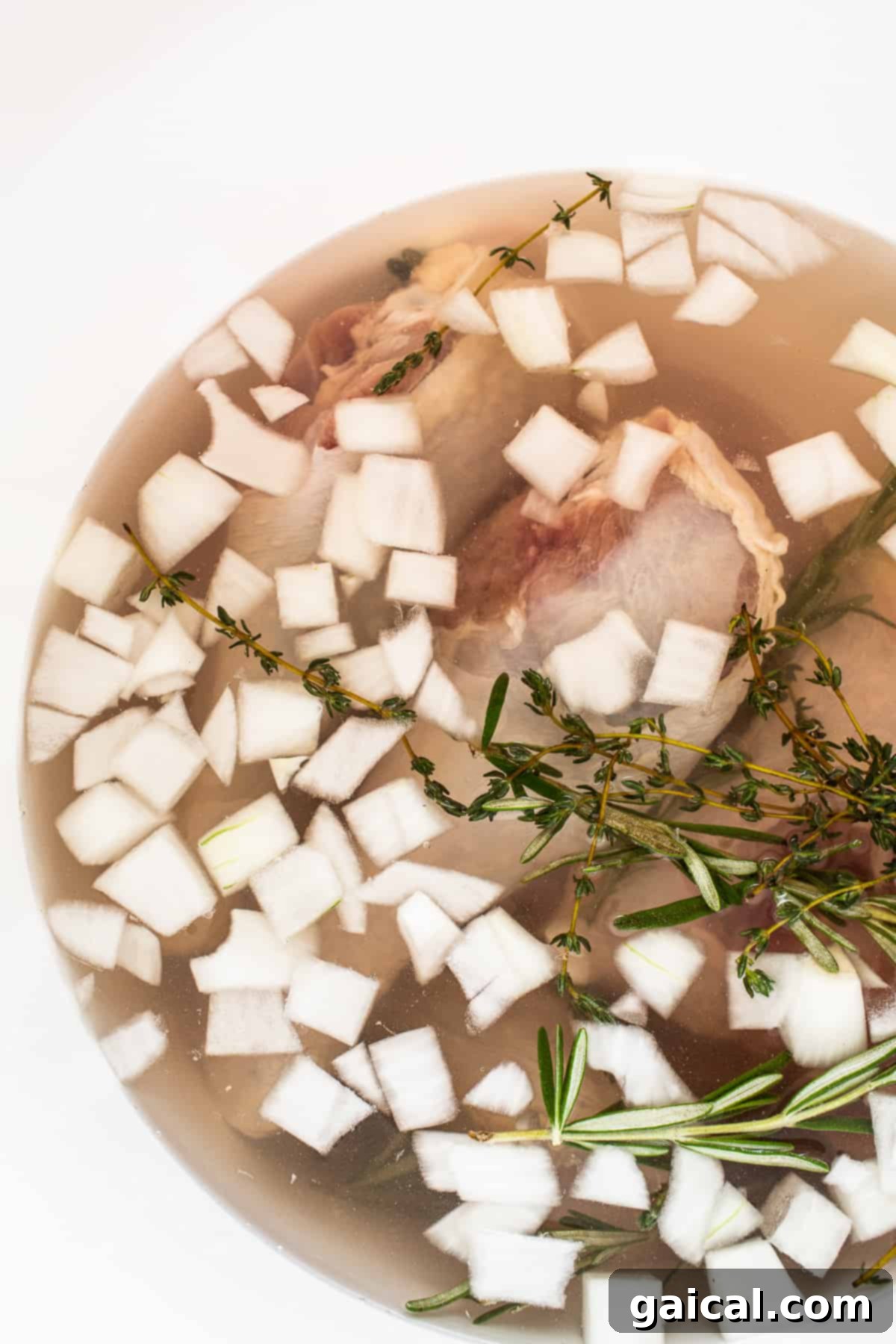 A whole turkey submerged in an herb and citrus-infused wet brine inside a large container, ready for chilling.