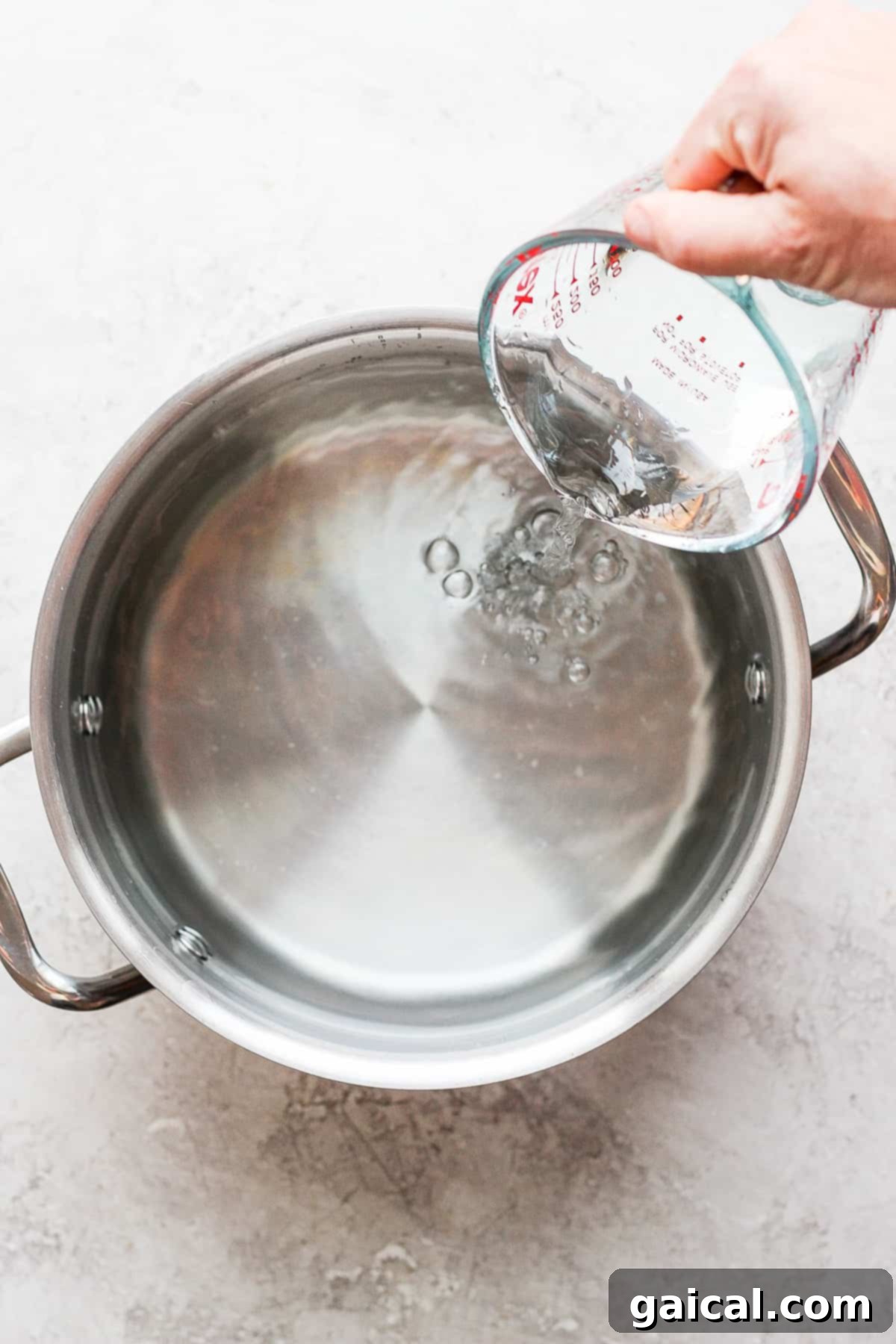 A hand adding fresh water into a large pot, preparing a wet brine solution.