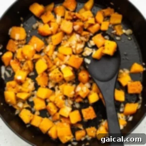 Squash cubes cooking in a skillet with a black spoon, developing a rich caramelization.