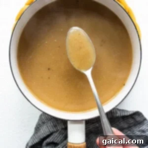 Velvety Homemade Turkey Gravy 4 A person holding a spoon, checking the consistency of thickening gravy in a pot on the stove.