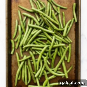 Roasted green beans on a baking sheet, mid-cooking process.