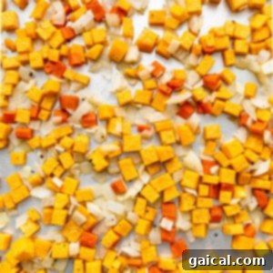 A pile of yellow and orange cubed vegetables on a baking sheet.