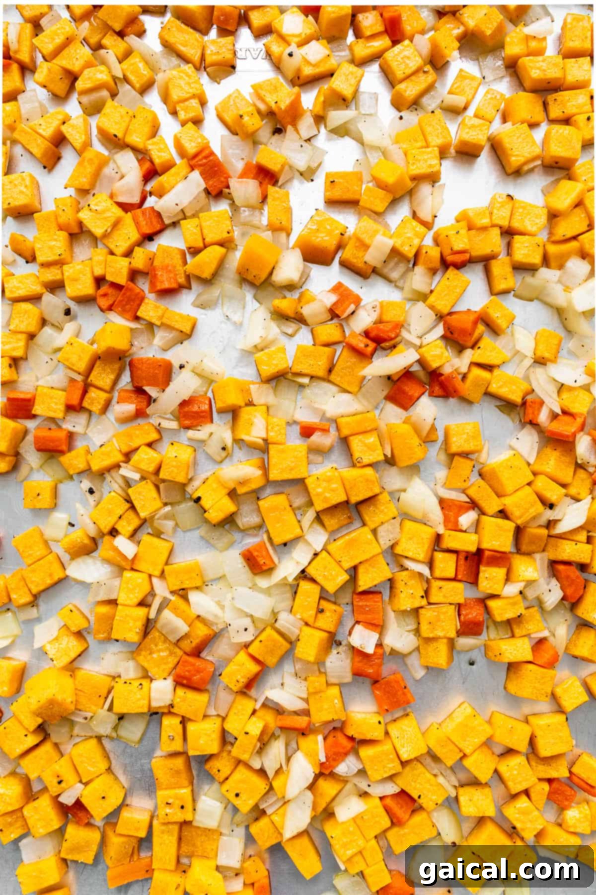 Roasted butternut squash, carrots, and onions on a baking sheet, glistening with olive oil.