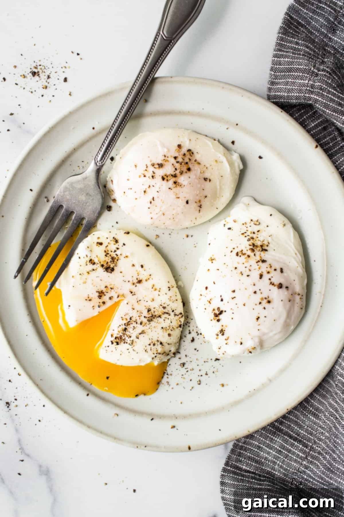 Achieve the perfect runny yolk with firm whites using our easy poached egg recipe. Two perfectly poached eggs on a plate with a fork, showing a runny yolk.