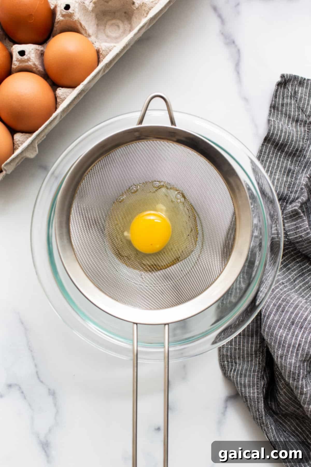 Strain your eggs for perfect poached whites. A raw egg being strained through a fine mesh strainer, separating the loose whites.
