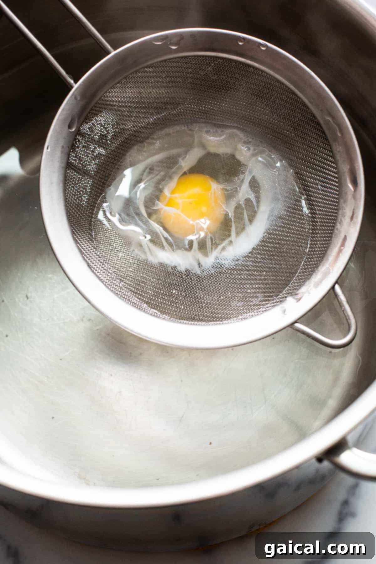 The crucial step of gently placing the strained egg into the poaching water. Another view of a raw egg in a mesh strainer being lowered into simmering water.