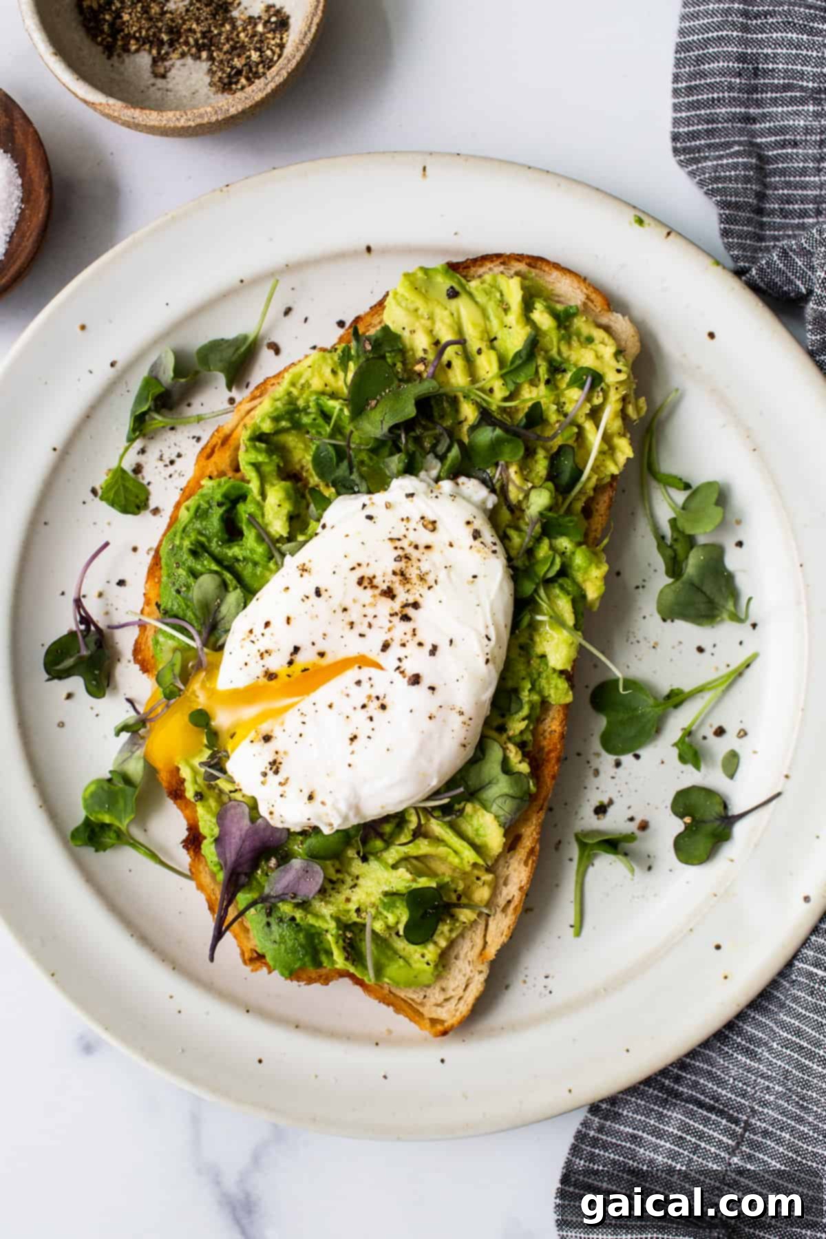 Poached egg on avocado toast with microgreens: a gourmet breakfast. A beautifully plated poached egg on avocado toast, garnished with fresh microgreens.
