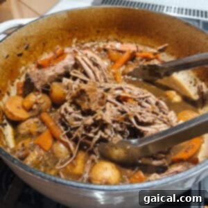 Slow-Cooked Tender Beef Roast 2 A savory pot roast stew with shredded beef, tender carrots, and potatoes simmering in a rich, flavorful broth inside a Dutch oven. Tongs are resting on the pot's edge, ready to serve.