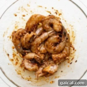 Shrimp in a glass bowl on a white surface, soaking in marinade.