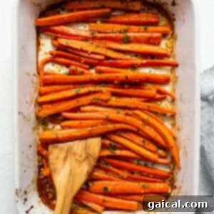 Roasted carrots in a baking dish with a wooden spoon.