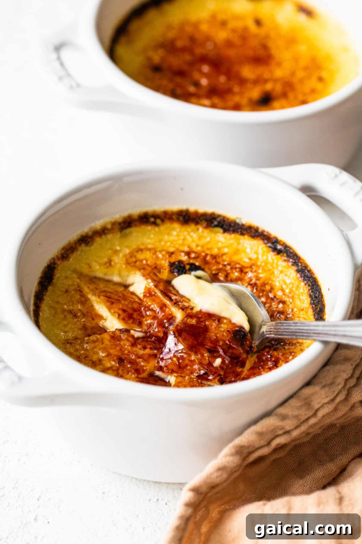 Spiced Eggnog Crème Brûlée 8 A spoon breaking through the caramelized top of an Eggnog Crème Brûlée.