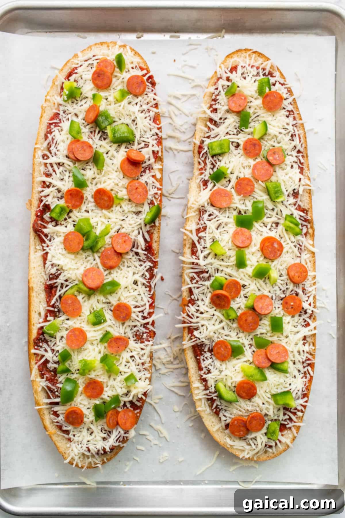 Assembled French Bread Pizza Ready for the Oven Two halves of Italian bread assembled with pizza sauce, cheese, pepperoni, and green peppers on a baking sheet, ready to bake.