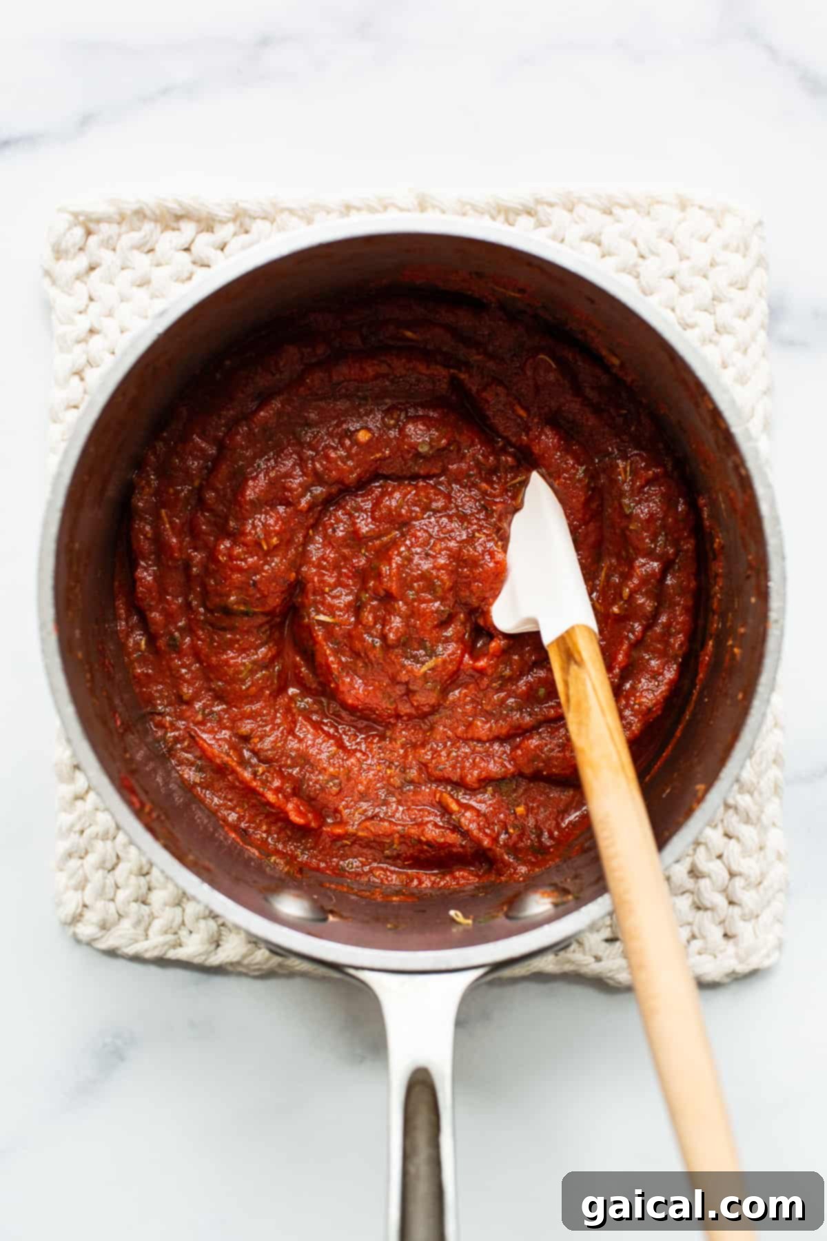 Simmering Homemade Pizza Sauce for Optimal Flavor Homemade pizza sauce simmering in a saucepan with a wooden spoon.