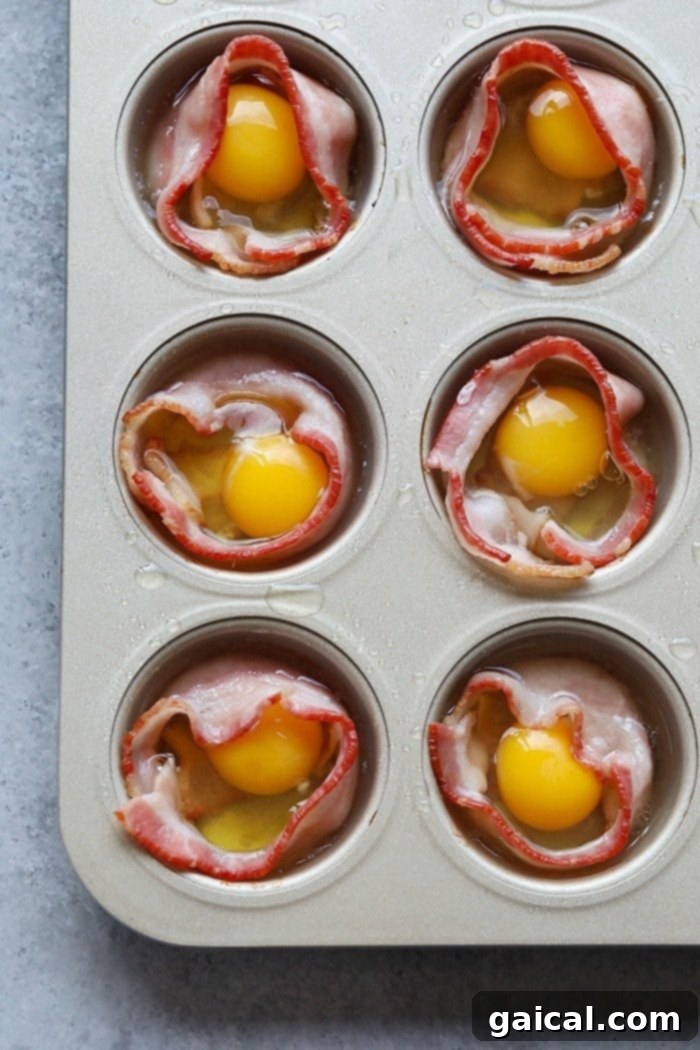 15+ Creative Egg Breakfasts to Kickstart Your Day 11 Raw eggs being carefully cracked into the center of bacon-lined muffin cups, ready for baking.