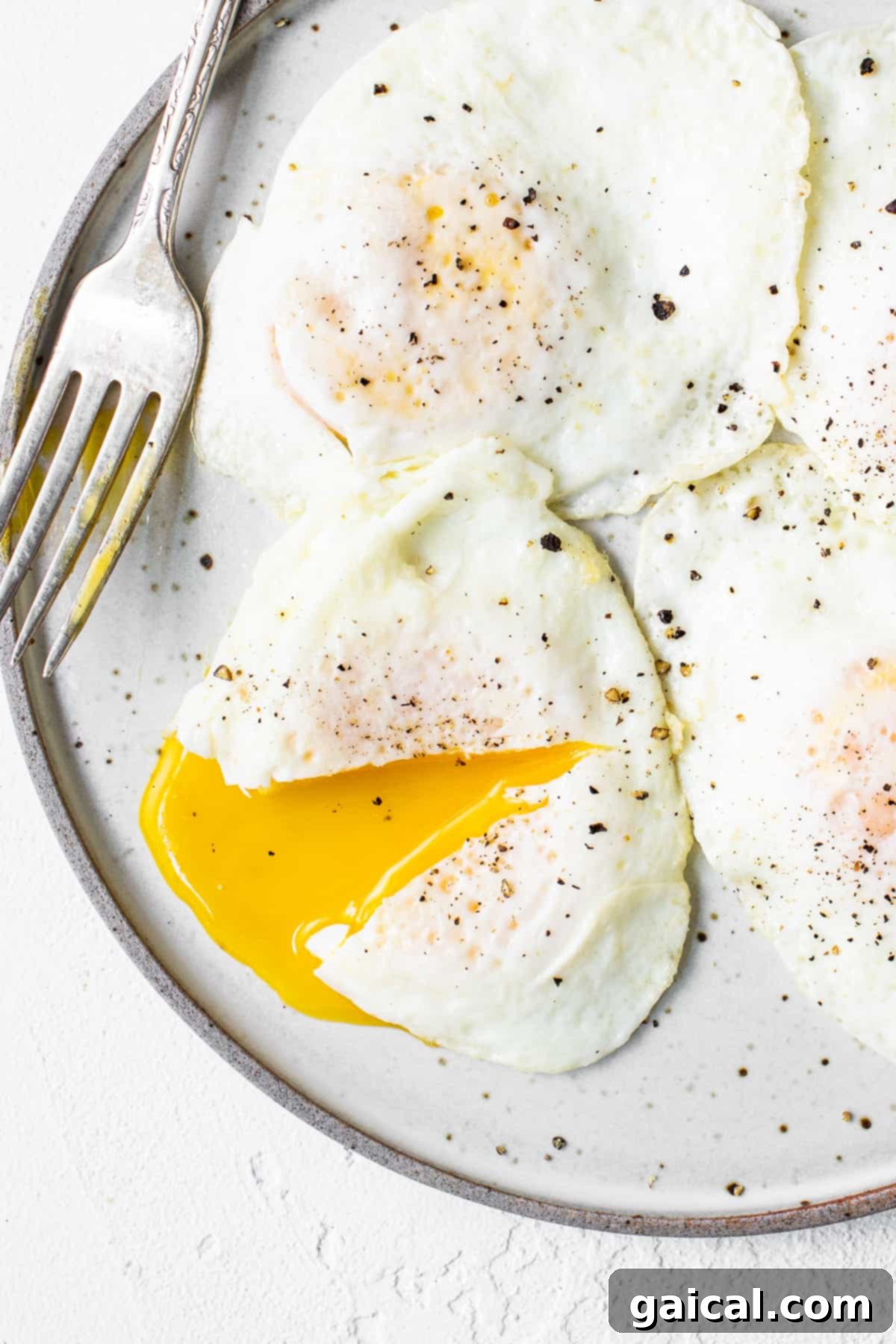 Liquid Gold Breakfast 2 Two over easy eggs on a plate with a fork, ready to be enjoyed.