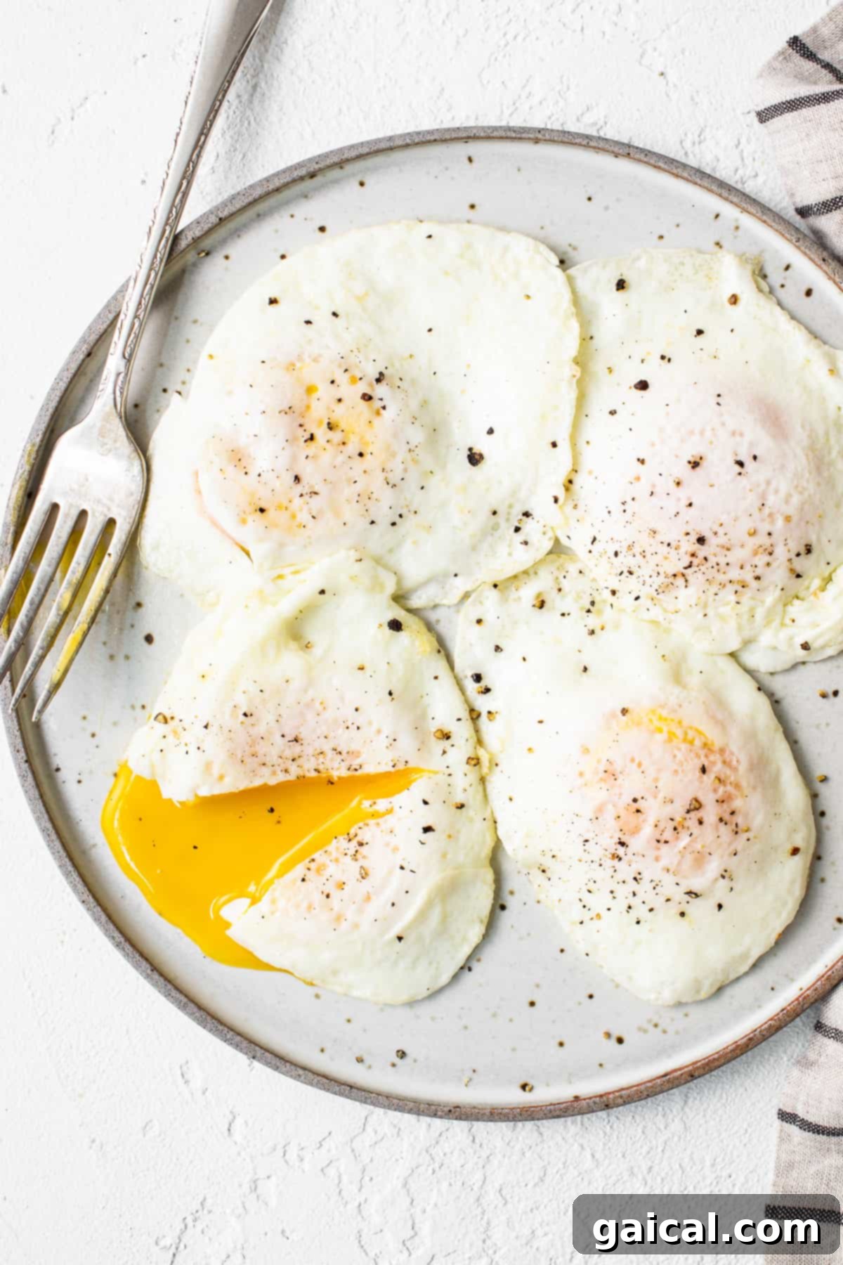 Liquid Gold Breakfast 7 Four perfectly cooked over easy eggs on a white plate, ready to be served.