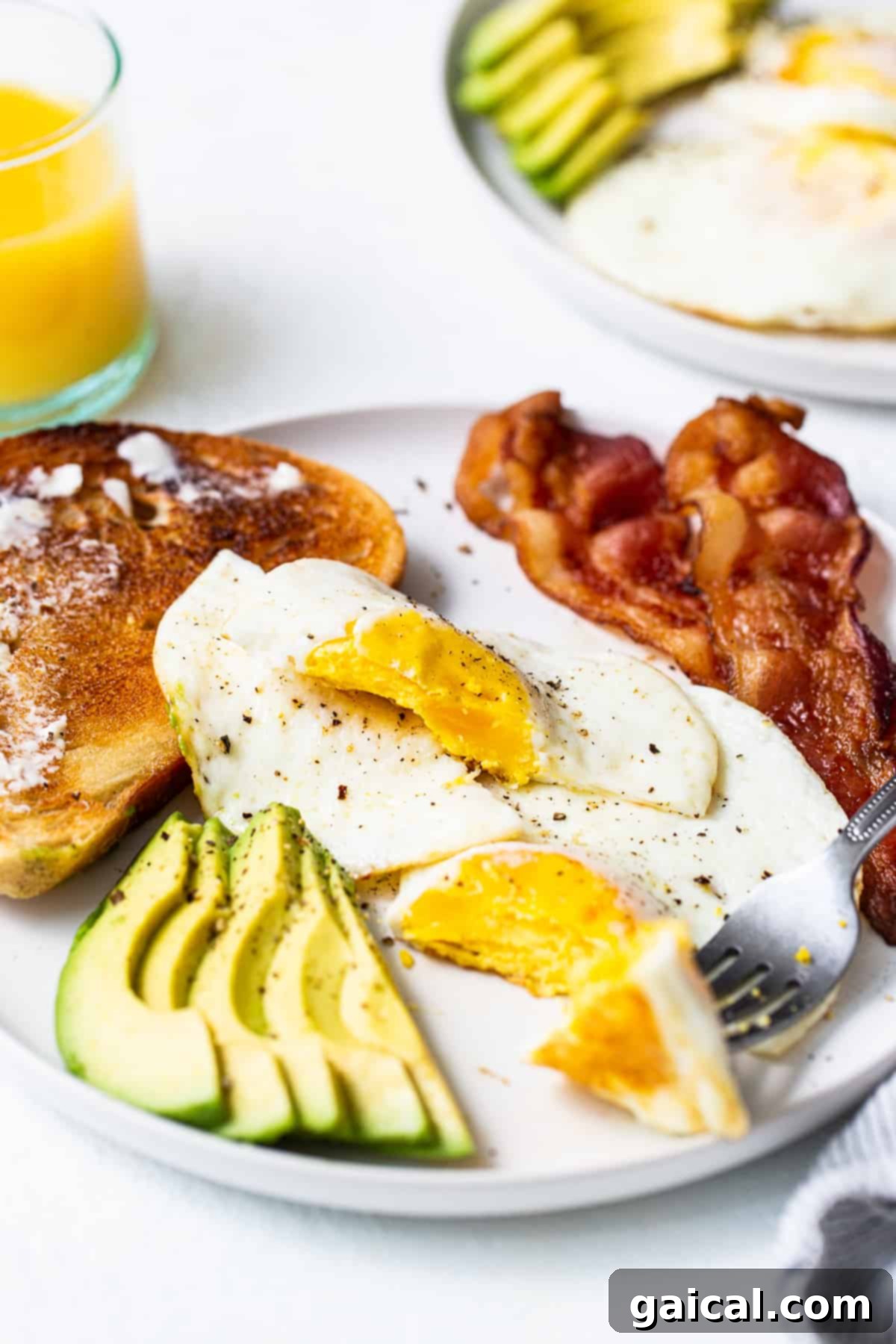 Two over hard eggs served on a white plate alongside crispy bacon slices, ready for a satisfying breakfast.
