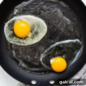 Two fresh eggs cracking into a hot, buttered frying pan.
