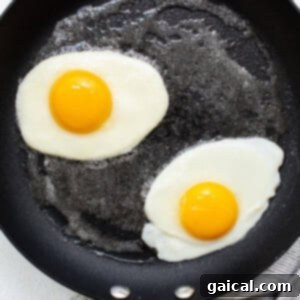 Two fried eggs with whites setting in a frying pan.