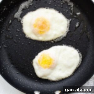 Two fried eggs flipped and cooking in a frying pan.