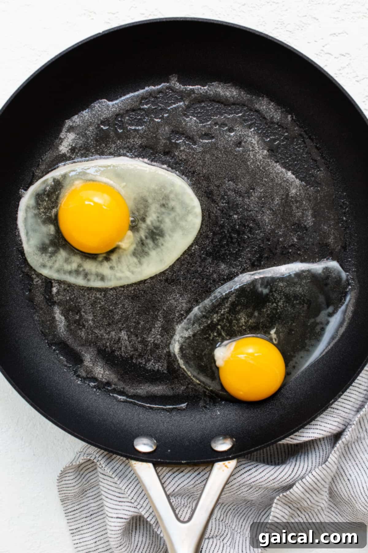 Two over hard eggs sizzling gently in a non-stick skillet, their whites opaque and yolks beginning to firm.