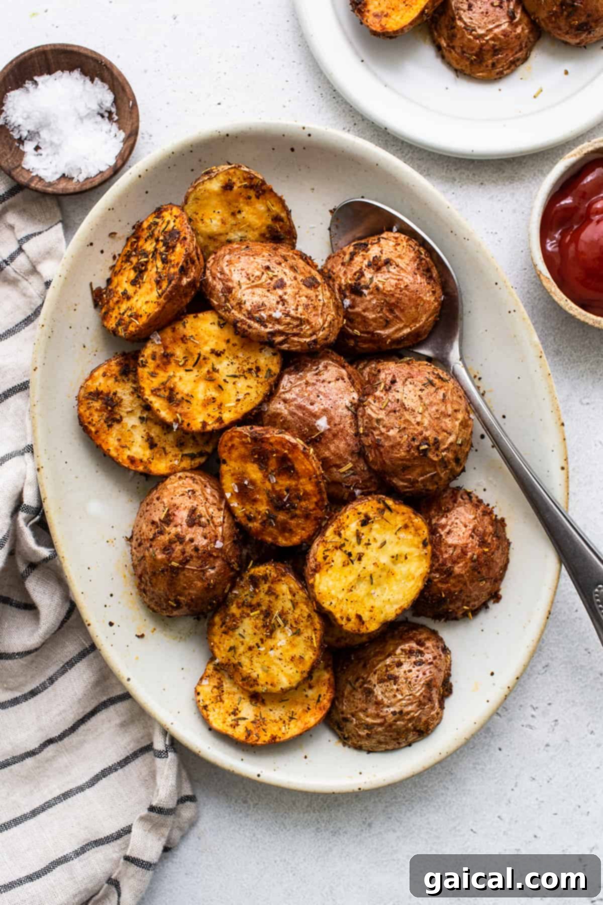 A close-up shot of perfectly cooked air fryer potatoes on a plate, garnished with fresh herbs, alongside a serving spoon.