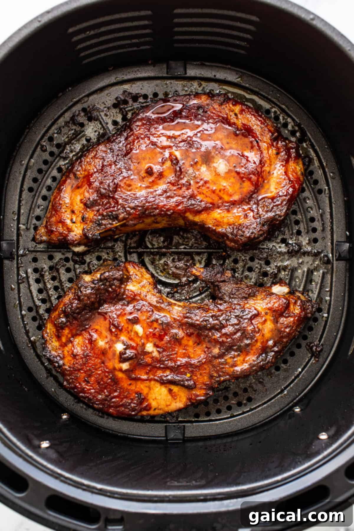 Pork Chops Cooking in Air Fryer Two golden-brown air fryer pork chops in the air fryer basket, showcasing their crispy exterior.