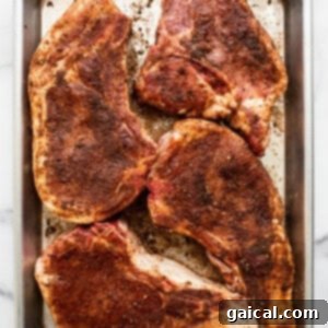 Succulent Air Fried Pork Chops 3 Raw pork chops seasoned with dry rub on a baking sheet, preparing for the air fryer.