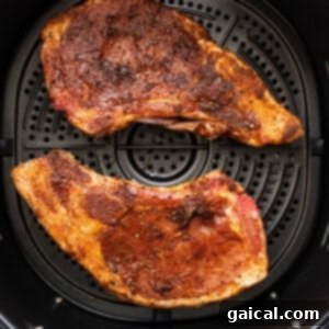 Succulent Air Fried Pork Chops 4 Two seasoned pork chops cooking in an air fryer basket, achieving a golden-brown sear.