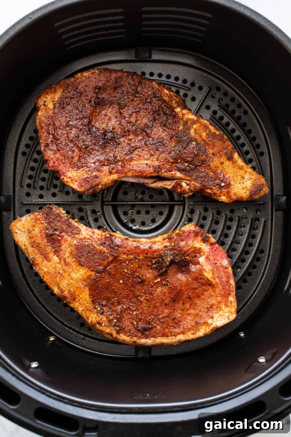 Pork Chops in Air Fryer Two golden-brown pork chops cooking inside an air fryer basket, steam rising slightly.