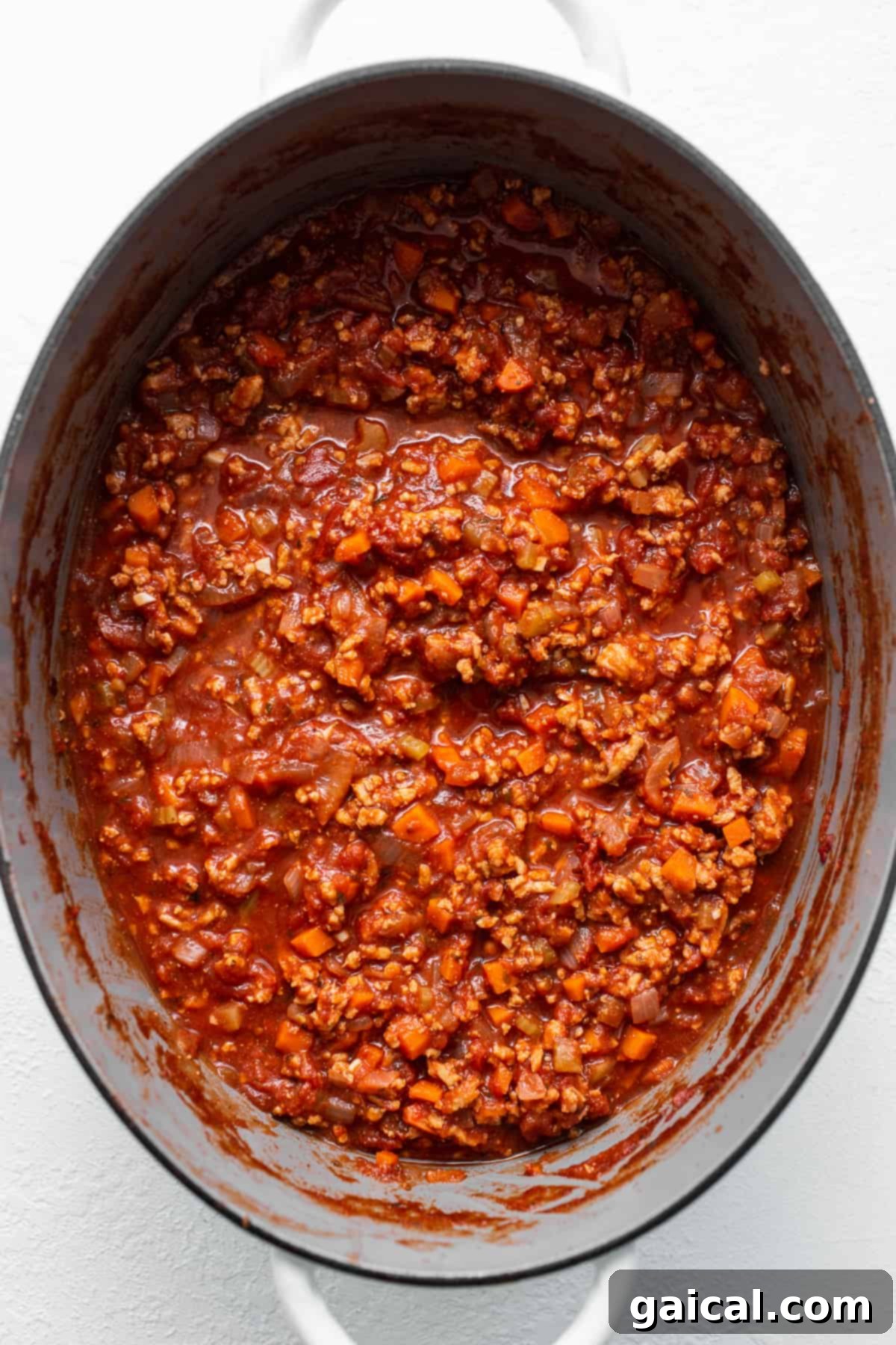 Ground chicken bolognese simmering to perfection. Rich ground chicken bolognese simmering in a large red Dutch oven, a cozy and inviting scene.