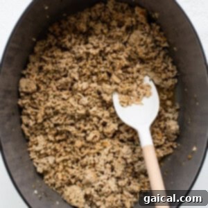 Ground chicken browning in a large Dutch oven with a wooden spoon, before spices are added.