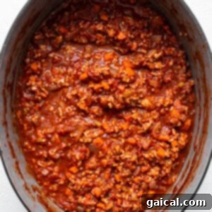Rich ground chicken bolognese simmering in a large red Dutch oven, a cozy and inviting scene.