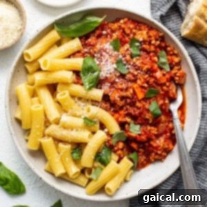 Ground chicken bolognese served in a bowl with freshly cooked pasta, garnished with herbs and cheese.