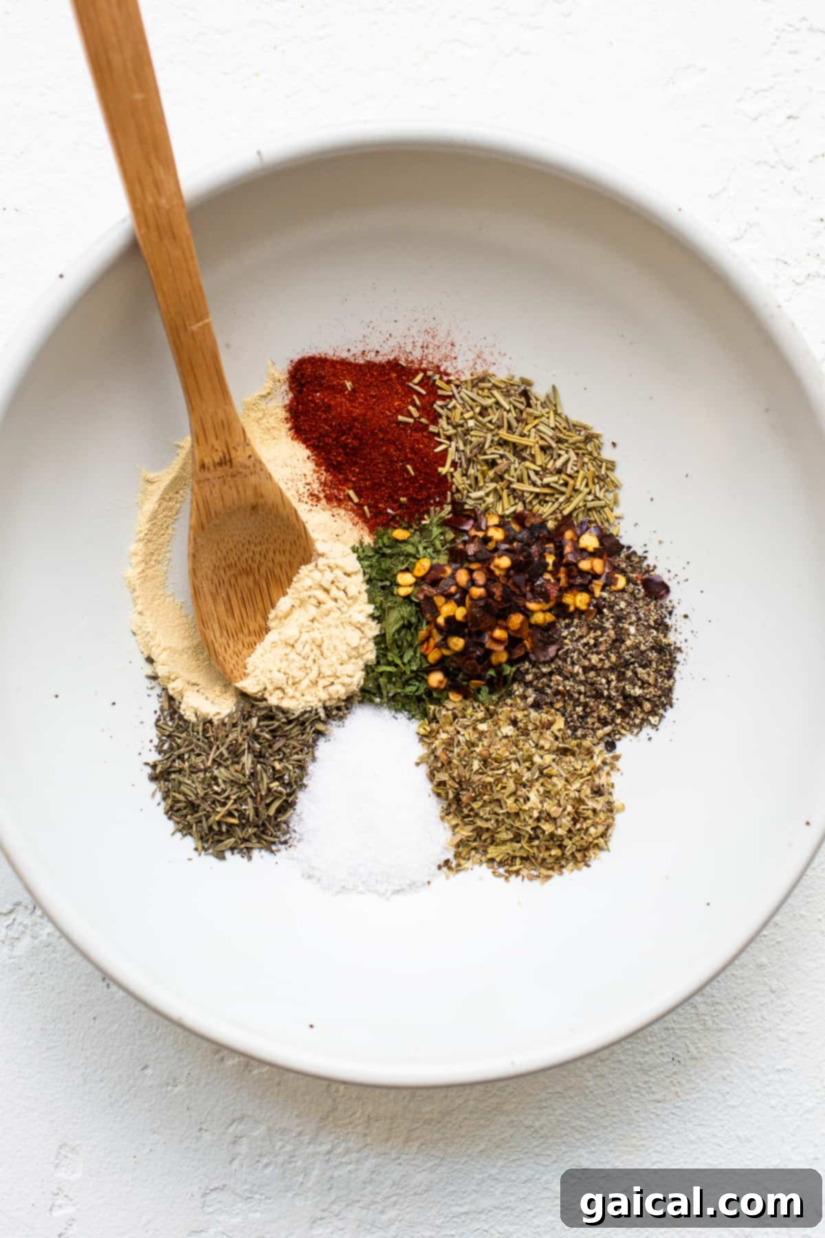 A fragrant blend of dried spices for our bolognese sauce. A small white bowl filled with a variety of dried spices for ground chicken bolognese, including paprika, thyme, rosemary, parsley, oregano, and red pepper flakes.