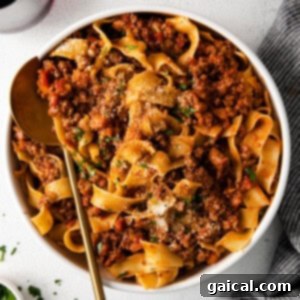 Wholesome Chicken Bolognese 2 A top-down view of slow cooker bolognese with pasta, garnished with fresh herbs and grated cheese.