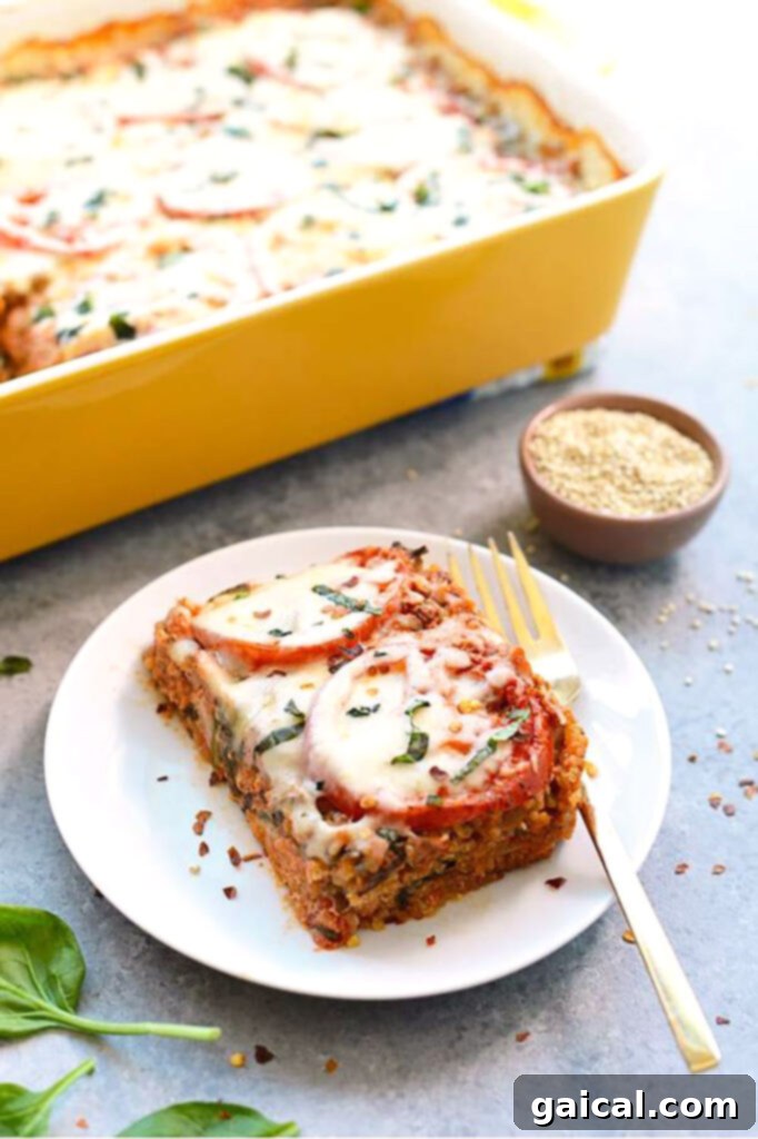 A perfectly portioned slice of quinoa lasagna on a white plate, accompanied by a fork.