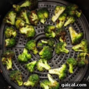Broccoli florets neatly arranged in an air fryer basket, halfway through cooking.