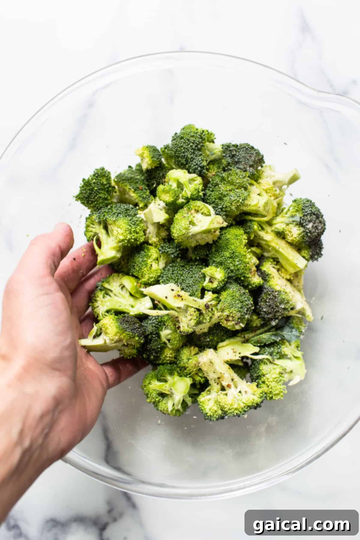 Fresh broccoli florets in a glass bowl, coated with olive oil and seasoning, ready for the air fryer.