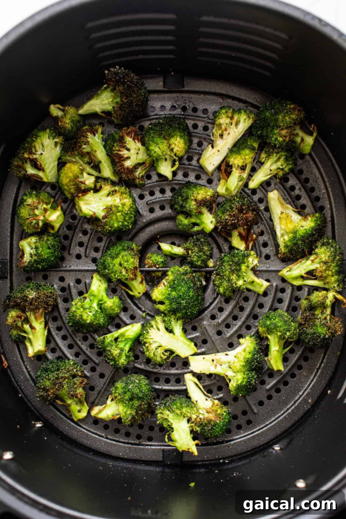 A close-up of crispy, golden-brown broccoli florets inside an air fryer basket, ready to be removed.