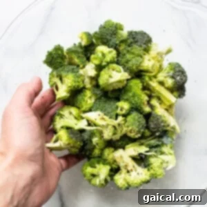 A person gently tossing and coating broccoli florets with seasoning and oil in a glass bowl.