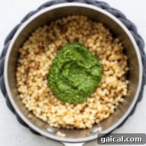 Warm Israeli couscous pearls expertly tossed with vibrant green kale pesto, infusing rich flavor.