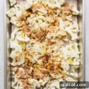 Thinly sliced cauliflower florets arranged on a baking sheet, seasoned with aromatic spices.