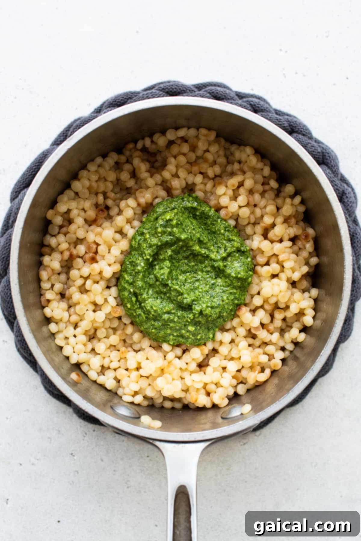 Fluffy Israeli couscous pearls gently tossed with a generous amount of green kale pesto in a bowl.